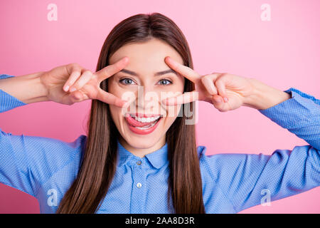 Close up foto di sorprendente lady mostra v-sign simboli vicino agli occhi leccare il labbro superiore di usura tratteggiata blu shirt isolato rosa pastello colore di sfondo Foto Stock