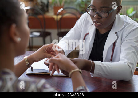 Black Girl - di un medico in camice bianco, con uno stetoscopio, prende il paziente. Razza mista il medico e il paziente Foto Stock