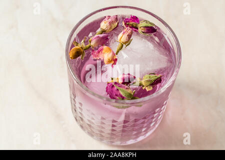 Pink gin tonic cocktail con secchi boccioli di rosa e il ghiaccio nel bicchiere di vetro. Pronto da bere. Foto Stock