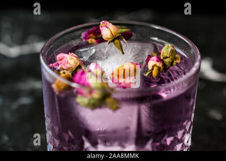 Pink gin tonic cocktail con secchi boccioli di rosa e il ghiaccio nel bicchiere di vetro. Pronto da bere. Foto Stock