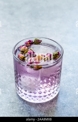 Pink gin tonic cocktail con secchi boccioli di rosa e il ghiaccio nel bicchiere di vetro. Pronto da bere. Foto Stock