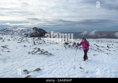 Walker avvicinarsi al vertice di Scafell Pike in inverno con la montagna di Castle e la costa a Sellafield oltre, Lake District, Cumbria, Regno Unito Foto Stock