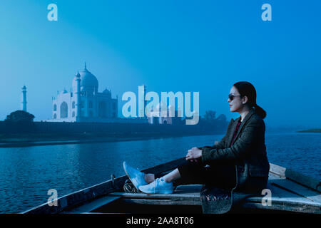 Donna seduta sulla barca di legno nel fiume Yamuna con Taj Mahal in background. Foto Stock