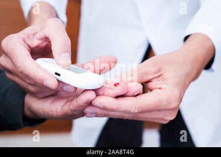 Primo piano di una giovane caucasico uomo medic, indossando il camice bianco, circa per misurare il livello di glucosio nel sangue di un vecchio uomo caucasico in un misuratore di glucosio Foto Stock