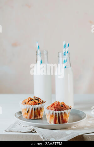 Vaniglia e caramello muffin in bicchieri di carta e botlles di latte bianco su sfondo di legno. Deliziosa tortina con uvetta, mandorle e noci. Biscu fatti in casa Foto Stock