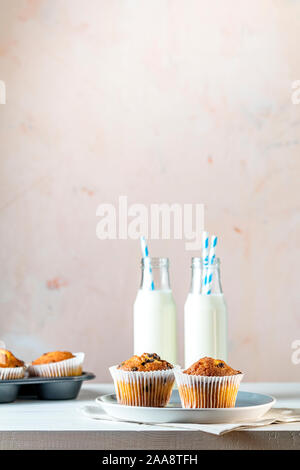 Vaniglia e caramello muffin in bicchieri di carta e botlles di latte bianco su sfondo di legno. Deliziosa tortina con uvetta, mandorle e noci. Biscu fatti in casa Foto Stock