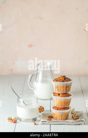 Vaniglia e caramello muffin in bicchieri di carta e bicchiere di latte bianco su sfondo di legno. Deliziosa tortina con uvetta, mandorle e noci. Biscotti fatti in casa Foto Stock