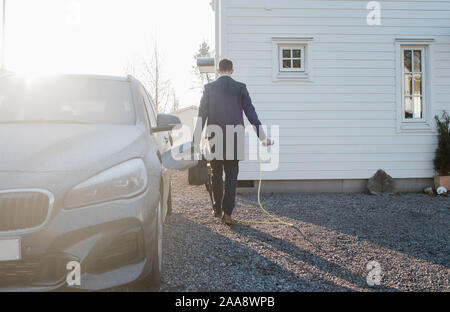 Uomo che cammina con auto elettrica filo lasciando al lavoro la mattina Foto Stock