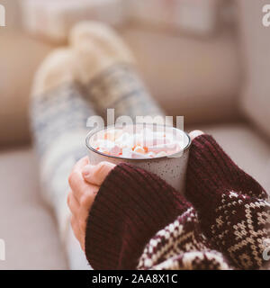 La donna in un maglione pesante con motivi e divertenti calzini di bere cioccolata calda Foto Stock