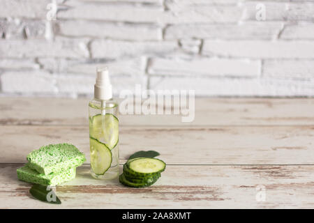 In casa del viso rinfrescante cetriolo toner in bottiglia con fette di cetriolo verde e cotone-pad bianco su sfondo di legno. Copia dello spazio. Foto Stock