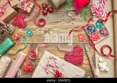 Sfondo di natale con confezioni regalo, nastri e rotoli di carta, decorazioni e candy canes sul tavolo di legno. Preparazione per le vacanze. Vista da sopra con copia Foto Stock