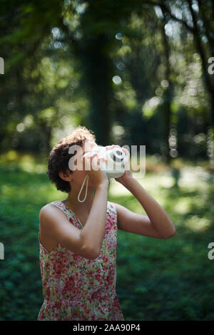 Entusiasta ragazza preteen sollevamento fotocamera istantanea e prendendo la foto in parco verde Foto Stock