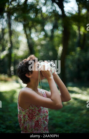 Entusiasta ragazza preteen sollevamento fotocamera istantanea e prendendo la foto in parco verde Foto Stock