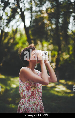 Entusiasta ragazza preteen sollevamento fotocamera istantanea e prendendo la foto in parco verde Foto Stock