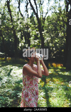 Entusiasta ragazza preteen sollevamento fotocamera istantanea e prendendo la foto in parco verde Foto Stock