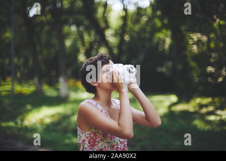 Entusiasta ragazza preteen sollevamento fotocamera istantanea e prendendo la foto in parco verde Foto Stock