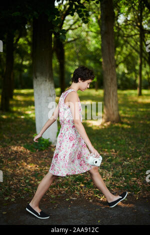 Adorabile ragazza preteen tenendo la fotocamera istantanea e passeggiate nel parco verde Foto Stock