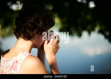 Entusiasta ragazza preteen sollevamento fotocamera istantanea e prendendo la foto in parco verde Foto Stock