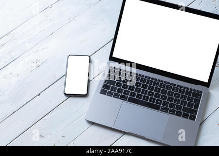 Il portatile e telefono con schermi in bianco su bianco tavolo in legno. Area di lavoro. Copia dello spazio. Foto Stock