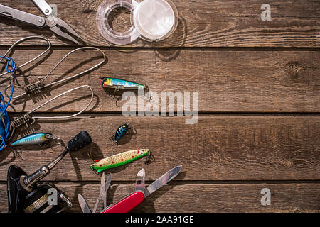 Accessori per la pesca sullo sfondo di legno. Aspo, la lenza, float, net ganci, esche artificiali per la pesca. Vista dall'alto. Ancora in vita. Spazio di copia Foto Stock