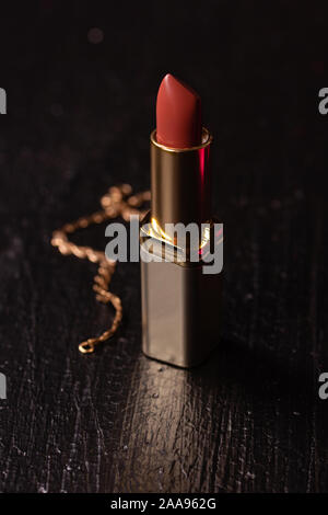 Bellissimo il rossetto in un tubo d'oro per il trucco su sfondo nero Foto Stock