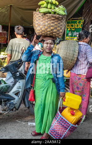 La vivace carne, pesce, frutta e verdura del mercato Pakokku, Myanmar (Birmania) come una giovane donna vende banane fresche da un carrello che porta sulla sua testa Foto Stock