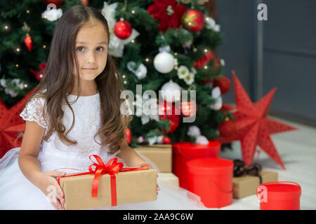 Bel bambino con un regalo di Natale. Medicazione ragazza fino al Nuovo Anno Albero.bambino indiano con scatola di natale Foto Stock