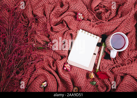 Composizione d'autunno. Tazza di tae, coperta, notebook con penna, rosa appassita. Appartamento laico, vista dall'alto, spazio di copia Foto Stock