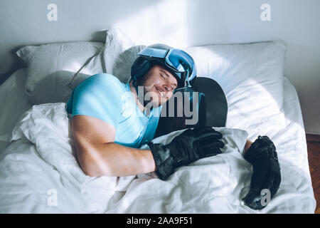 Uomo nel letto con lo snowboard ski googles e casco Foto Stock