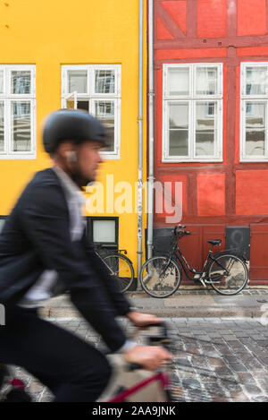 Copenhagen street view di un giovane uomo che indossa un casco ciclo escursioni in bicicletta attraverso il colorato centro storico quartiere del centro di Copenhagen, Danimarca. Foto Stock