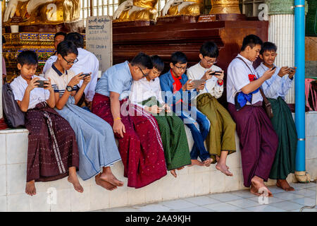 Giovani adolescenti birmano giocando con i loro telefoni cellulari alla Shwedagon pagoda Yangon, Myanmar. Foto Stock