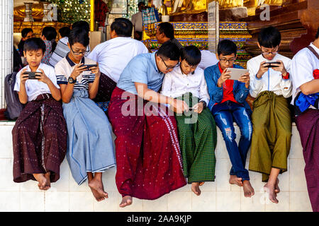 Giovani adolescenti birmano giocando con i loro telefoni cellulari alla Shwedagon pagoda Yangon, Myanmar. Foto Stock