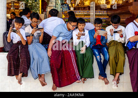 Giovani adolescenti birmano giocando con i loro telefoni cellulari alla Shwedagon pagoda Yangon, Myanmar. Foto Stock