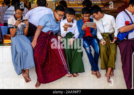 Giovani adolescenti birmano giocando con i loro telefoni cellulari alla Shwedagon pagoda Yangon, Myanmar. Foto Stock