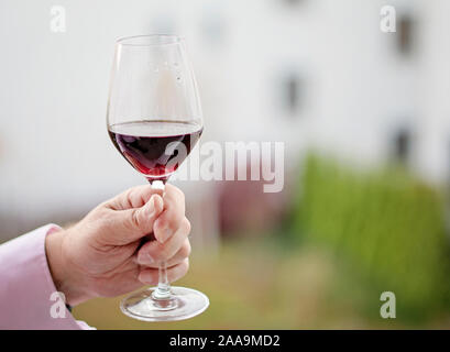 Mezzo bicchiere pieno di vino rosso in mano umana. Persona che tiene un bicchiere di vino. Copia spazio, spazio per il testo. Degustazione di vino costoso. Foto Stock