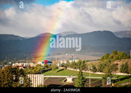 Fine di un arcobaleno nel cielo sopra il blocco di appartamenti in città con le montagne alle spalle. Cityscape Banska Bystrica, Slovacchia Foto Stock