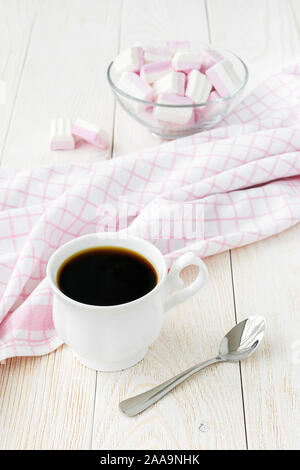 Tazza di caffè e di bianco rosa berry marshmallows in una ciotola di vetro sulla luce di un tavolo di legno. Dolce e gustoso cibo d'inverno. Deliziosi dolci morbidi. Foto Stock