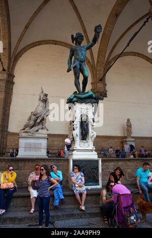 I turisti sedersi sotto la scultpure di Benvenuto Cellini di Perseo con la testa di Medusa, Loggia dei Lanzi, in Piazza della Signoria, Firenze, Italia Foto Stock