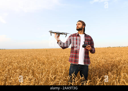 Tanga barbuto uomo mostra un piccolo drone compatto e mantiene il dispositivo di controllo remoto nella sua mano. Imprenditore agronomo guarda quadcopter prima del lancio in un Foto Stock