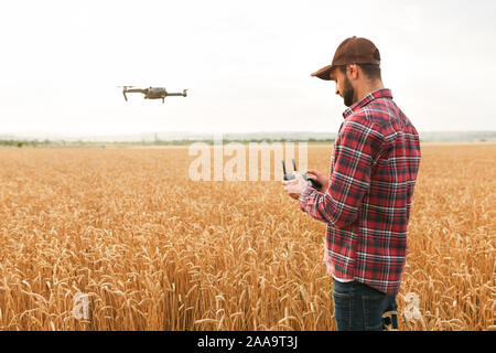 Agricoltore detiene remote controller con le sue mani mentre quadcopter è volare su sfondo. Drone vola dietro l'agronomo nel campo di grano Foto Stock