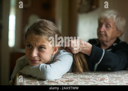 Old granny donna trecce una bambina's nipote capelli lunghi. Foto Stock