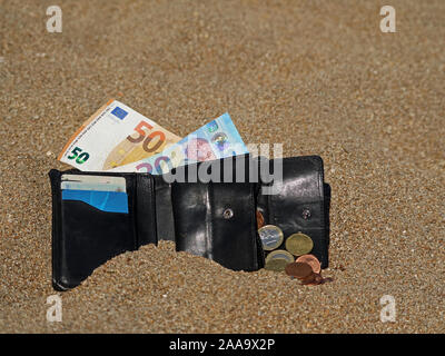 Aprire il portafoglio nero con le banconote e le monete in euro nella sabbia sulla spiaggia Foto Stock