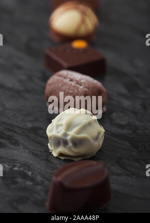 Il lusso di cioccolatini selezione sul pavimento di marmo nero a bordo. Bianco, cioccolato fondente e al latte assortimento. Macro Foto Stock