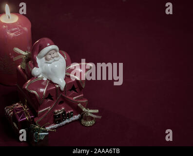 Ornamenti natalizi decorazione Babbo Natale e candela su sfondo rosso con spazio copia, foto-illustrazione Foto Stock