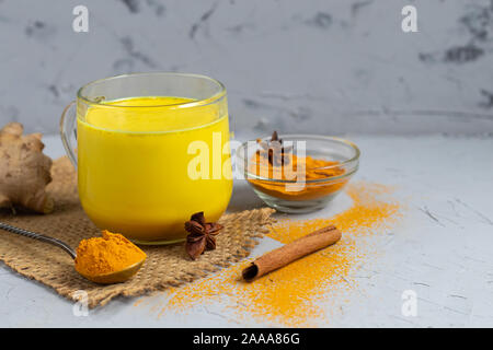 Golden latte con le spezie. La curcuma, chiodi di garofano e pepe nero e una goccia di olio vegetale. Tradizionale bevanda indiana. Su uno sfondo luminoso. Mangiare sano C Foto Stock