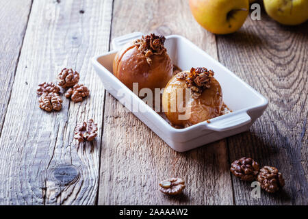 Vegan dessert, mele cotte con cereali integrali di avena, noci tritate, sciroppo d'acero sul tavolo di legno, impianto basato in autunno e inverno stagionali pasto vegano, clo Foto Stock
