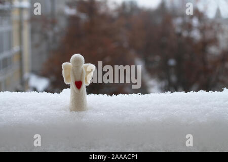 Giocattolo di lana angelo nella neve sulla ringhiera del balcone contro la strada. Dark giornata invernale Foto Stock
