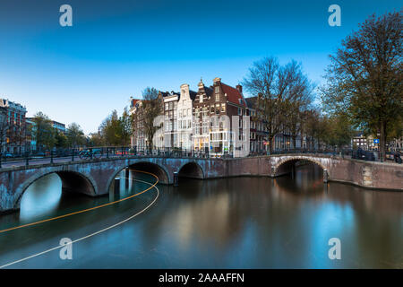 AMSTERDAM, Paesi Bassi - 30 Ottobre 2019: un ponte con luci sopra il canale Keizersgracht durante le ore di colore blu con strisce di luci in barca. Foto Stock