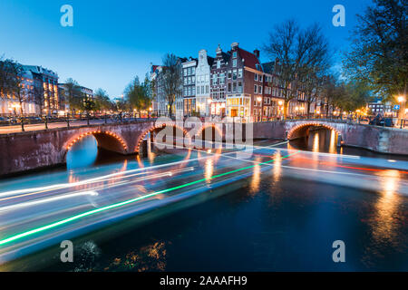 AMSTERDAM, Paesi Bassi - 30 Ottobre 2019: un ponte con luci sopra il canale Keizersgracht durante le ore di colore blu con strisce di luci in barca. Foto Stock