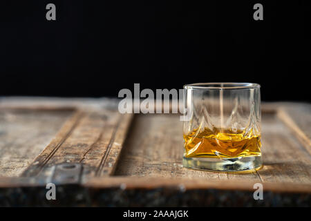 Whisky vetro su un vecchio usato tavolo in legno, sfondo scuro Foto Stock